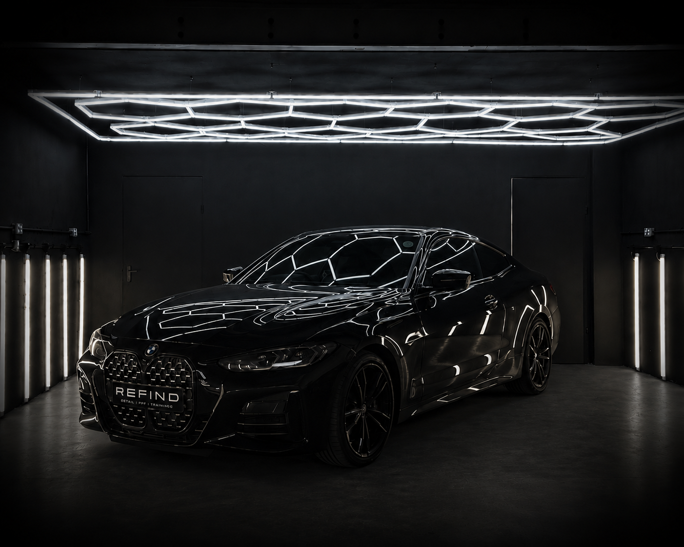 Black BMW 4 Series coupé under hexagonal studio lighting in a dark detailing studio